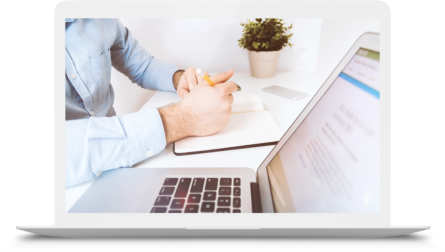 Mann schreibt etwas in sein Notizbuch während er etwas am am Laptop bearbeitet